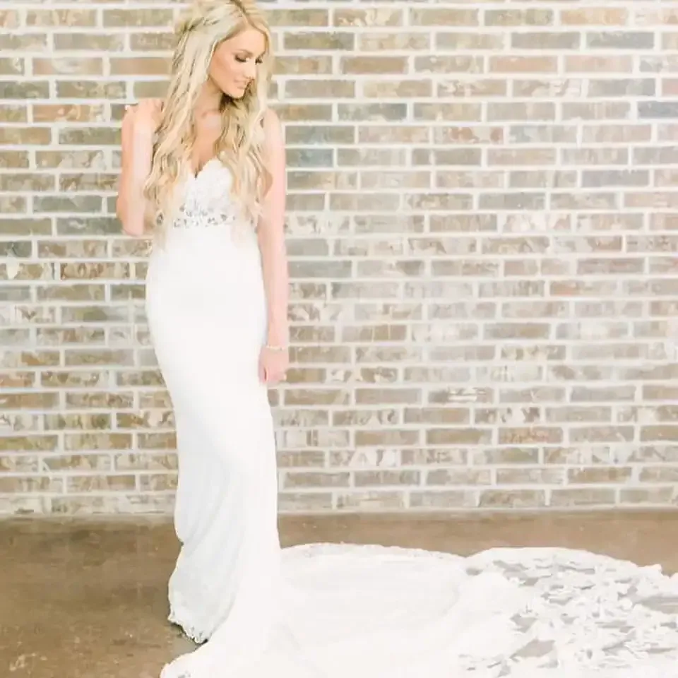 A woman in a white wedding dress is standing in front of a brick wall.