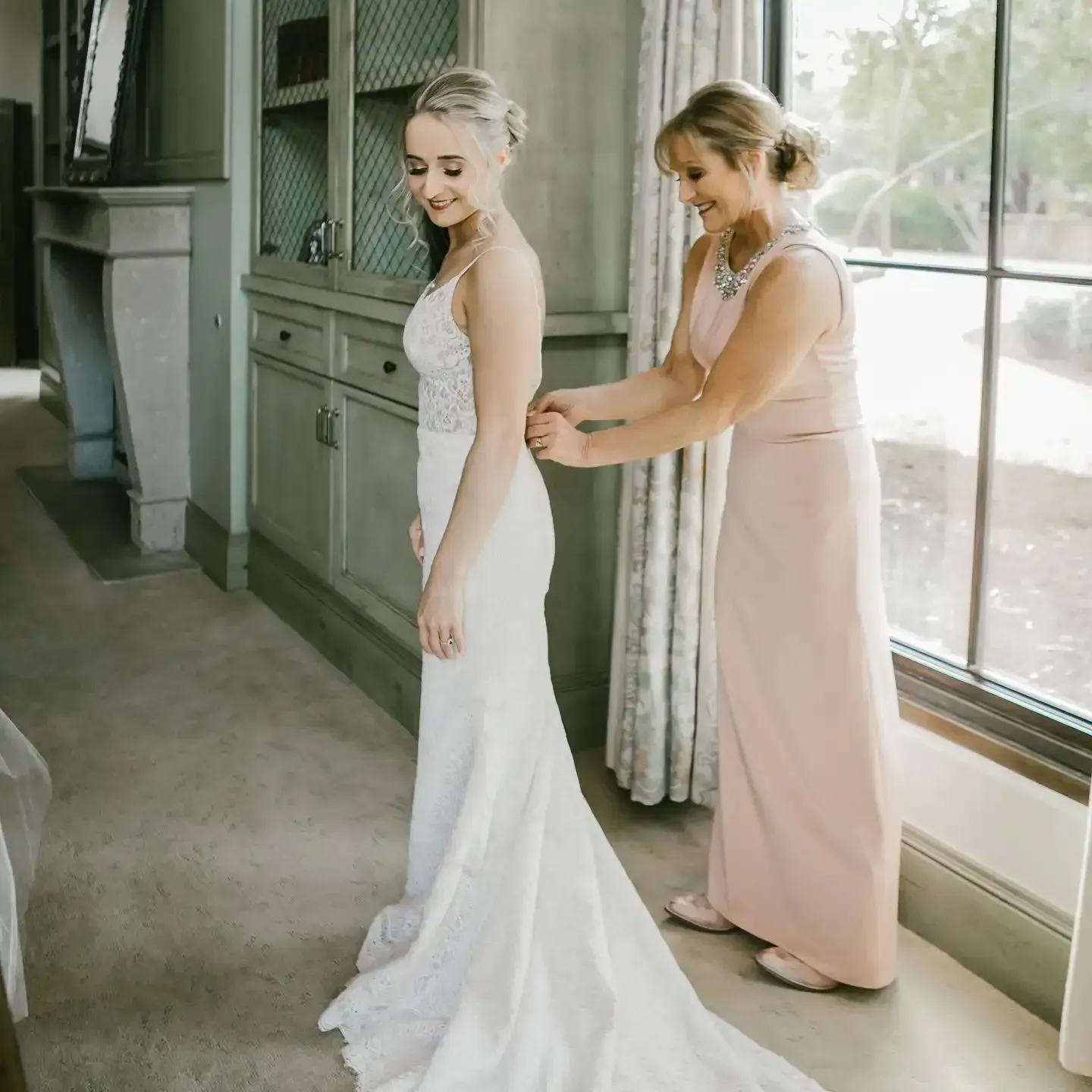 A woman in a pink dress helps a woman in a white dress