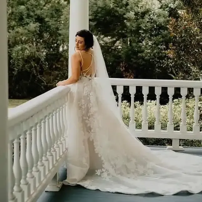A bride in a wedding dress and veil is standing on a porch.