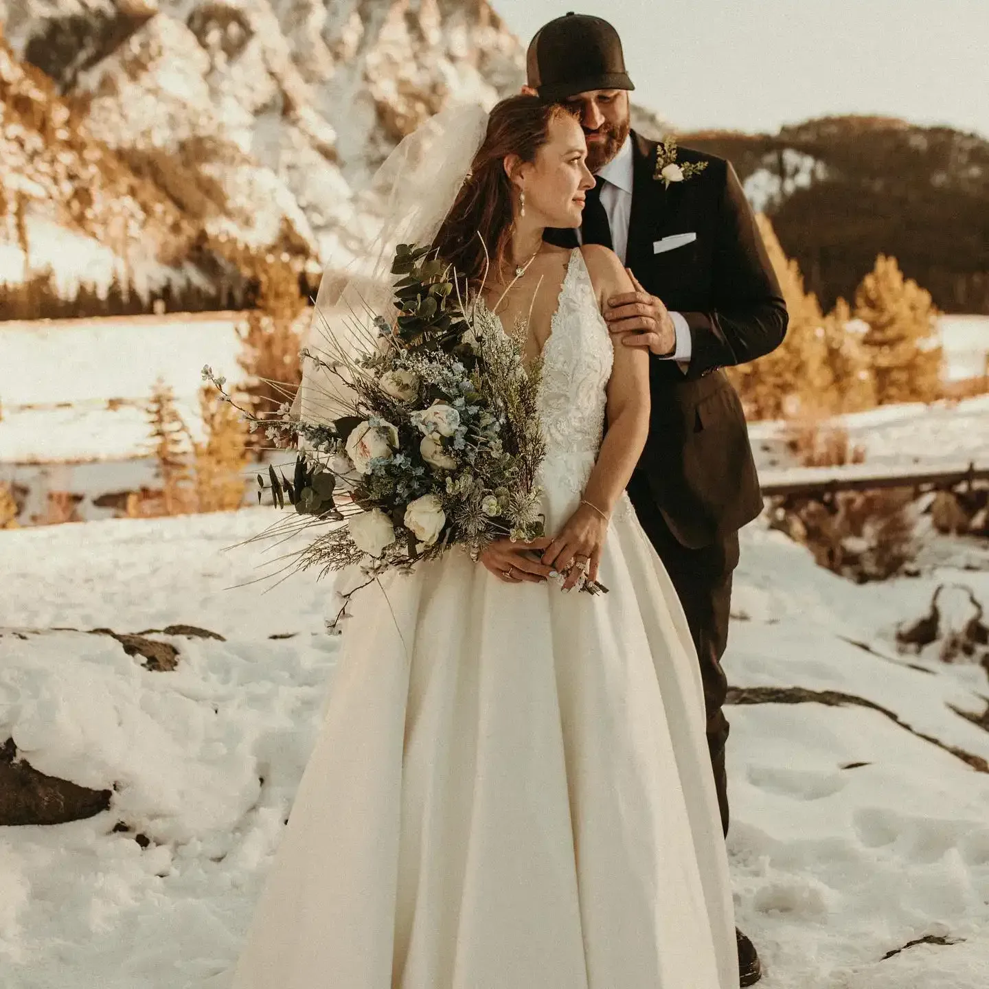 A bride and groom are posing for a picture in the snow.