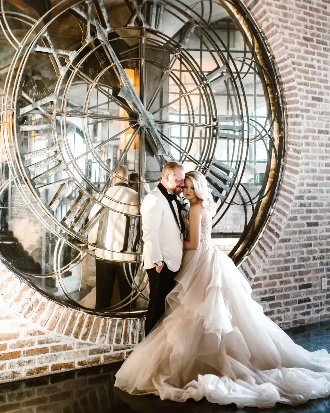 A bride and groom are posing for a picture in front of a large clock.