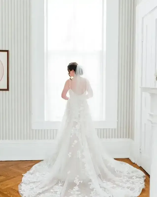 A bride in a wedding dress and veil is standing in front of a window.