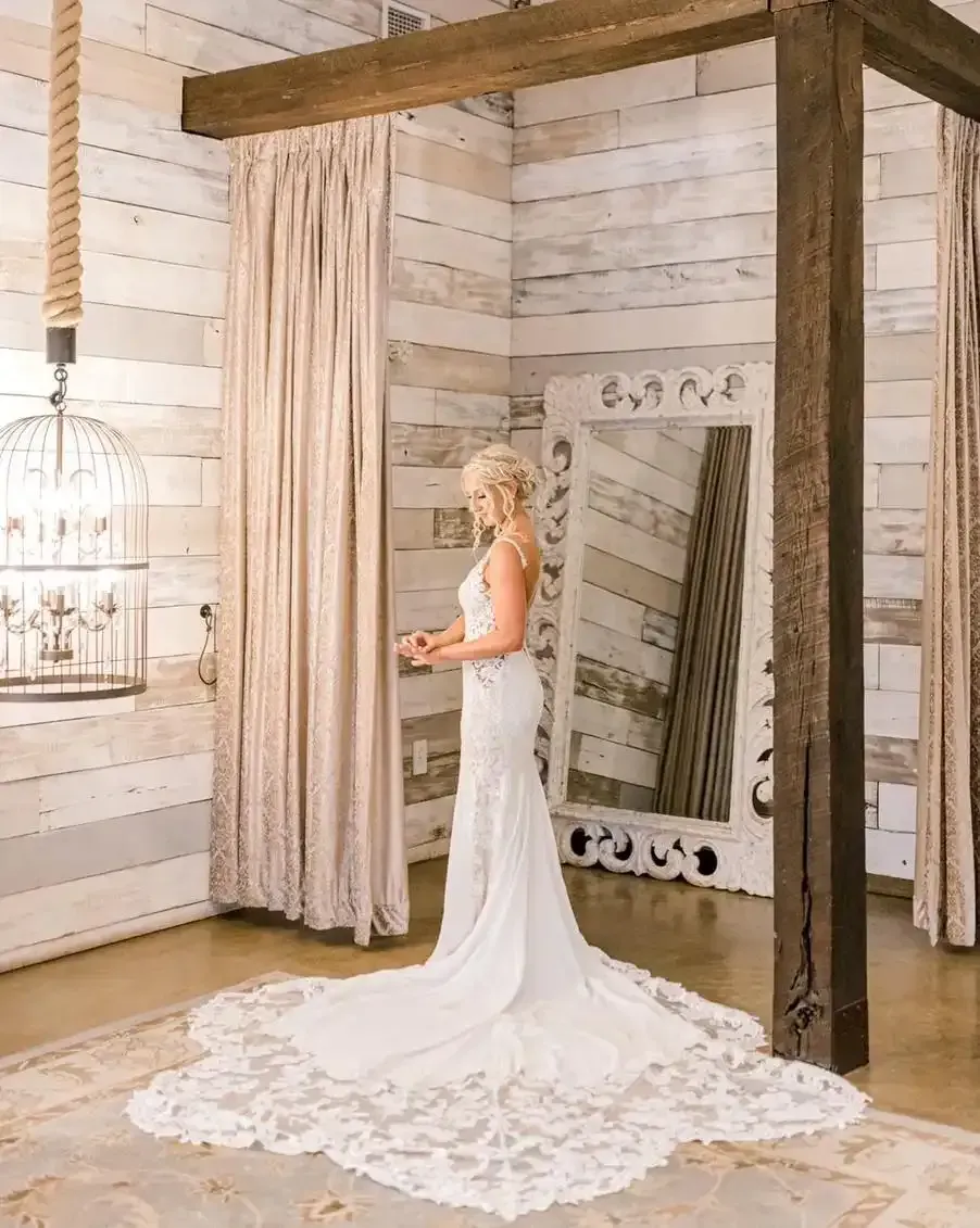 A woman in a wedding dress is standing in front of a mirror in a room.