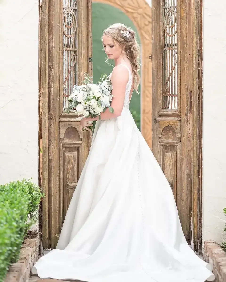 A bride in a wedding dress is standing in front of a wooden door holding a bouquet of flowers.