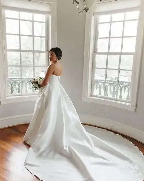 A bride in a white wedding dress is standing in front of a window.