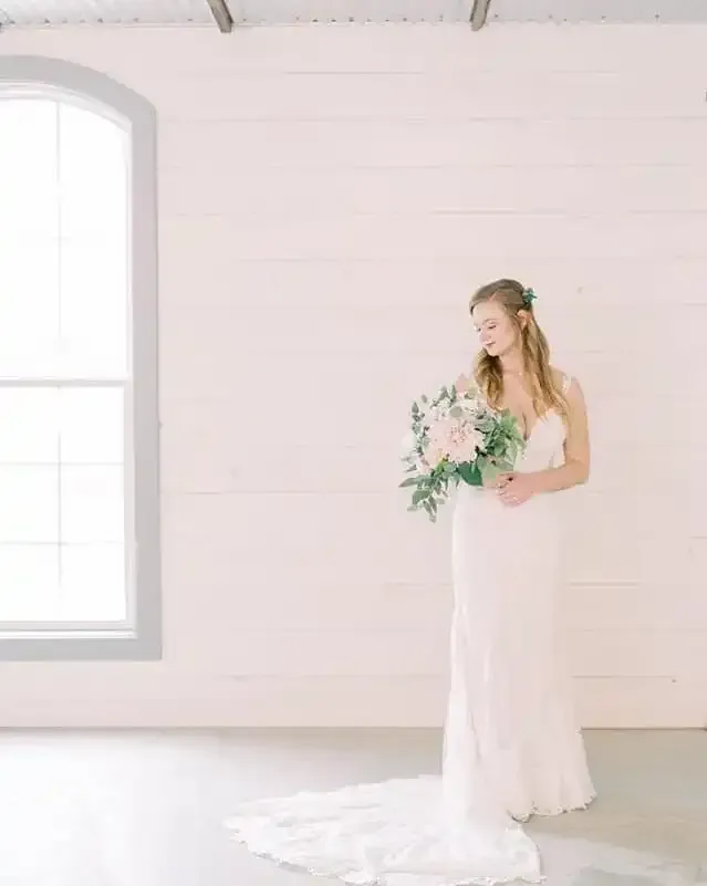 A bride in a wedding dress is standing in front of a window holding a bouquet of flowers.