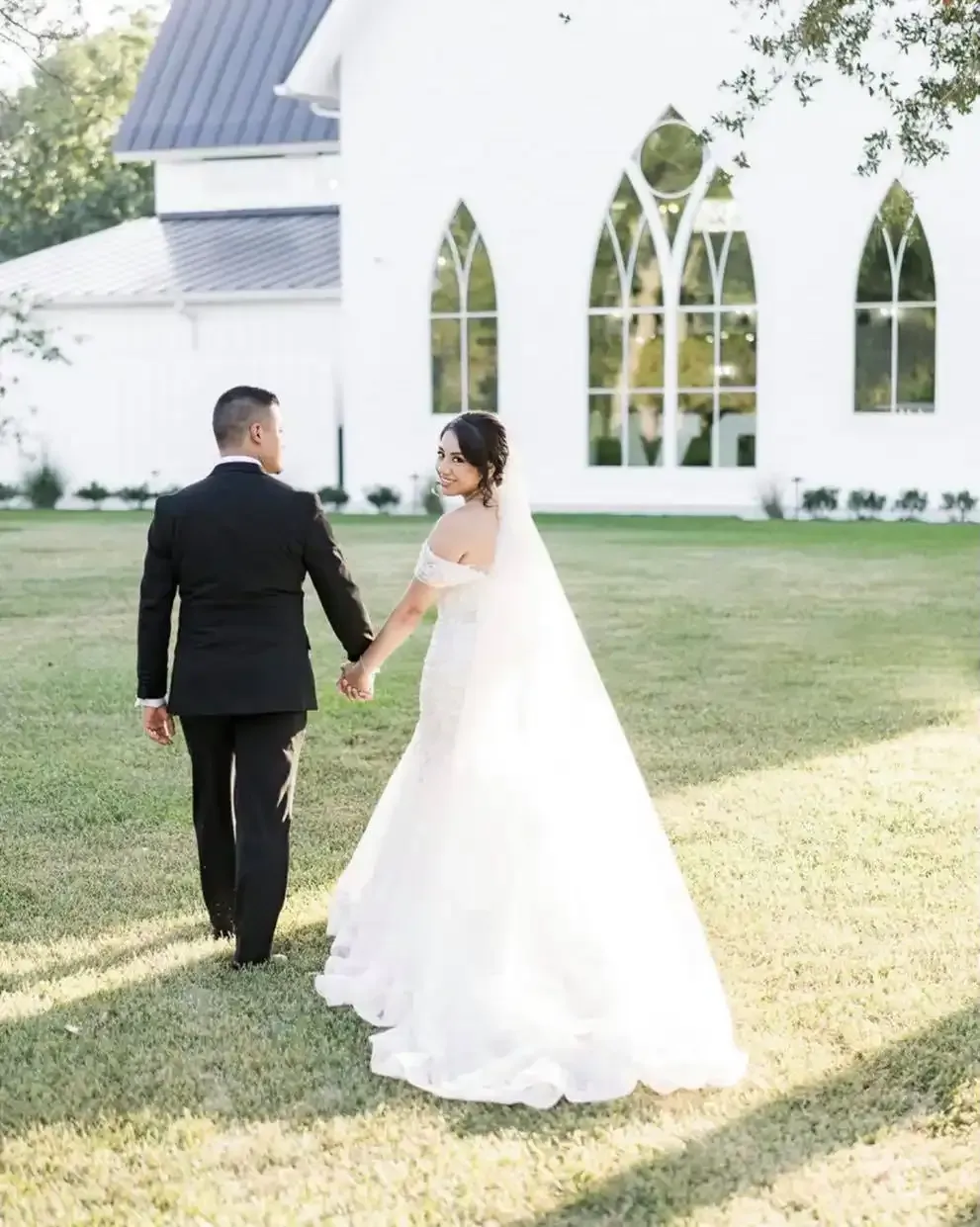 A bride and groom are walking in front of a white church holding hands.