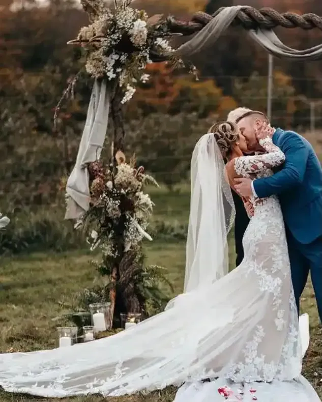 A bride and groom are kissing under a wooden arch.