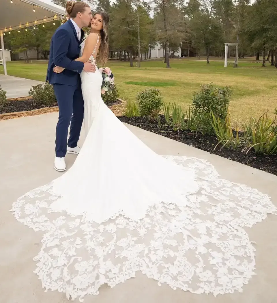 A bride and groom are kissing in front of a large lace train.