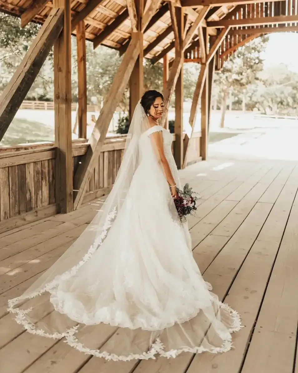 A bride in a wedding dress and veil is standing on a wooden bridge.