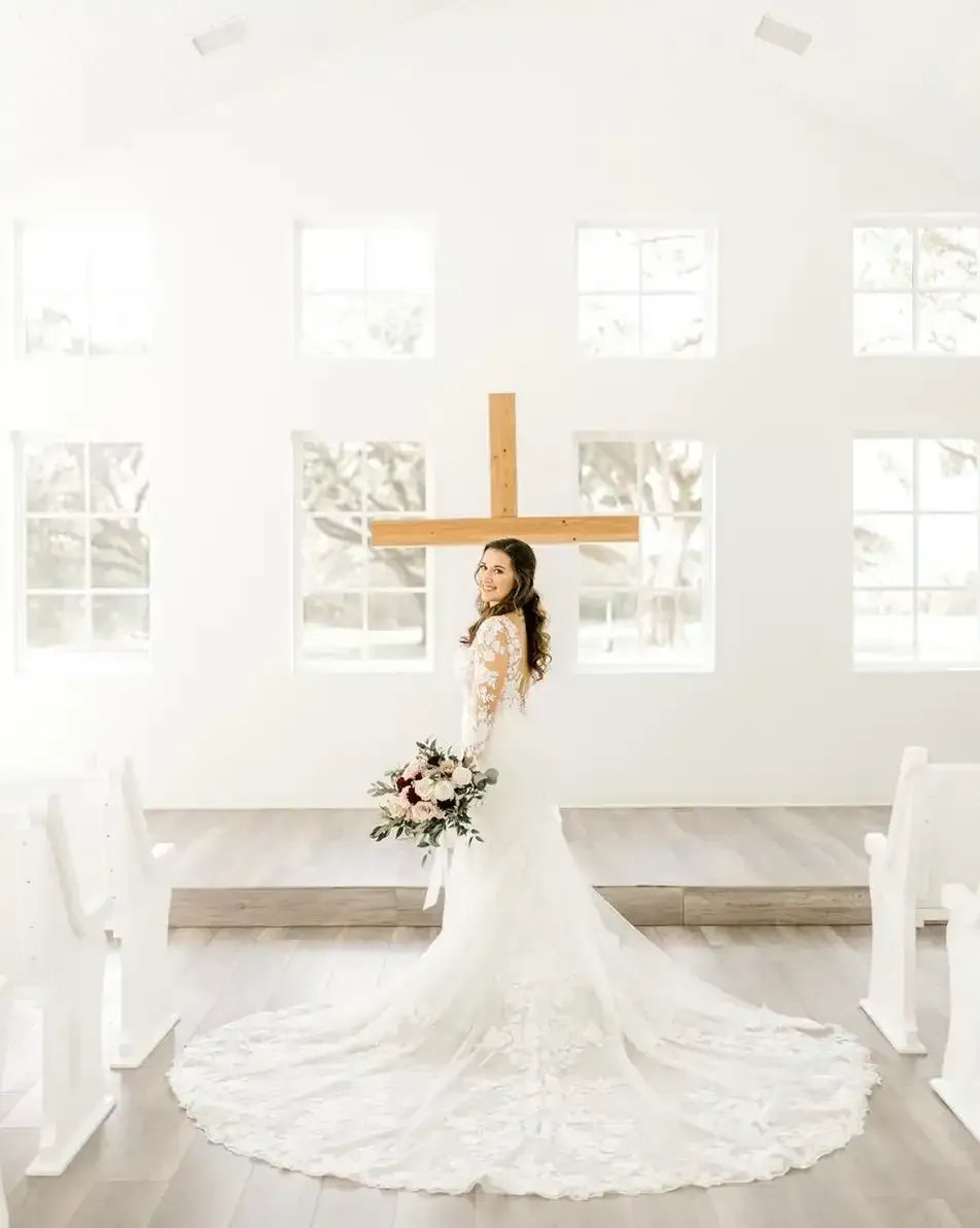 A bride in a wedding dress is standing in front of a cross in a church.