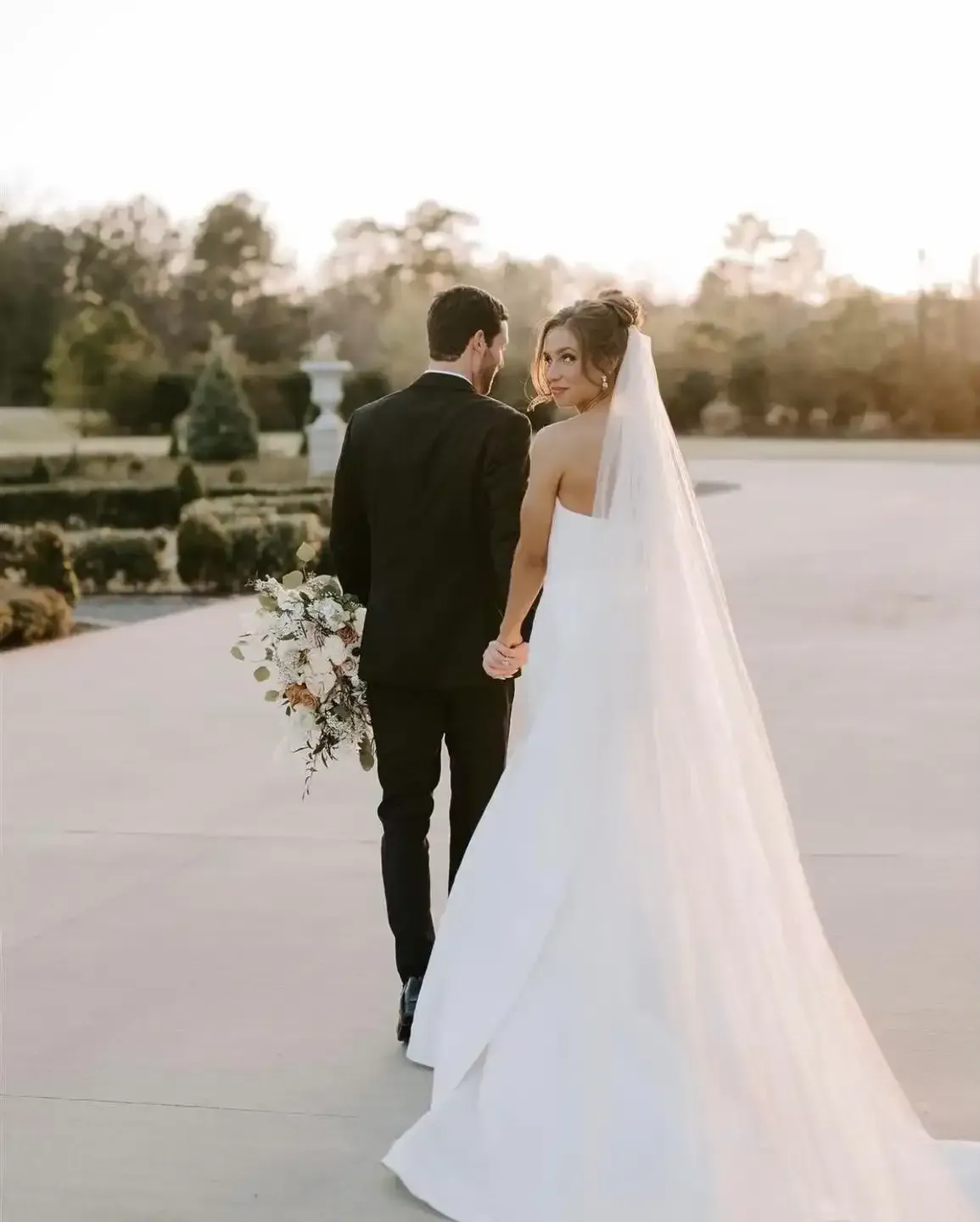 A bride and groom are walking down a sidewalk holding hands.