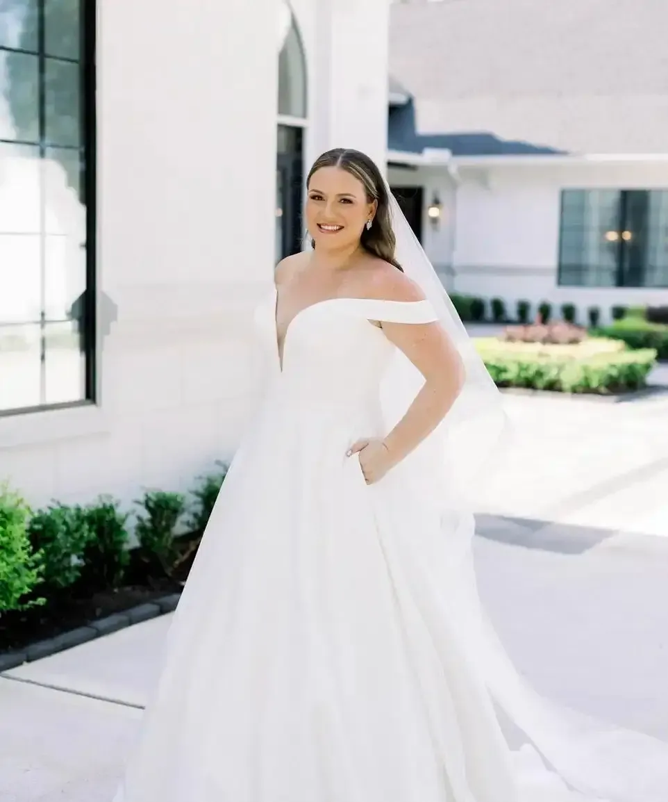 A bride in a white dress and veil is standing in front of a white building.