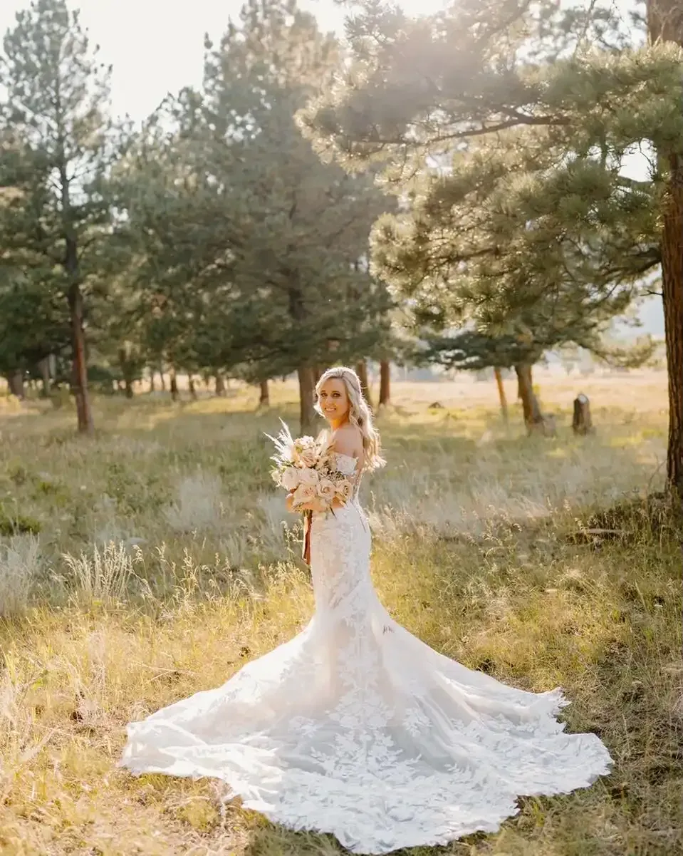 A bride in a wedding dress is standing in a field holding a bouquet of flowers.