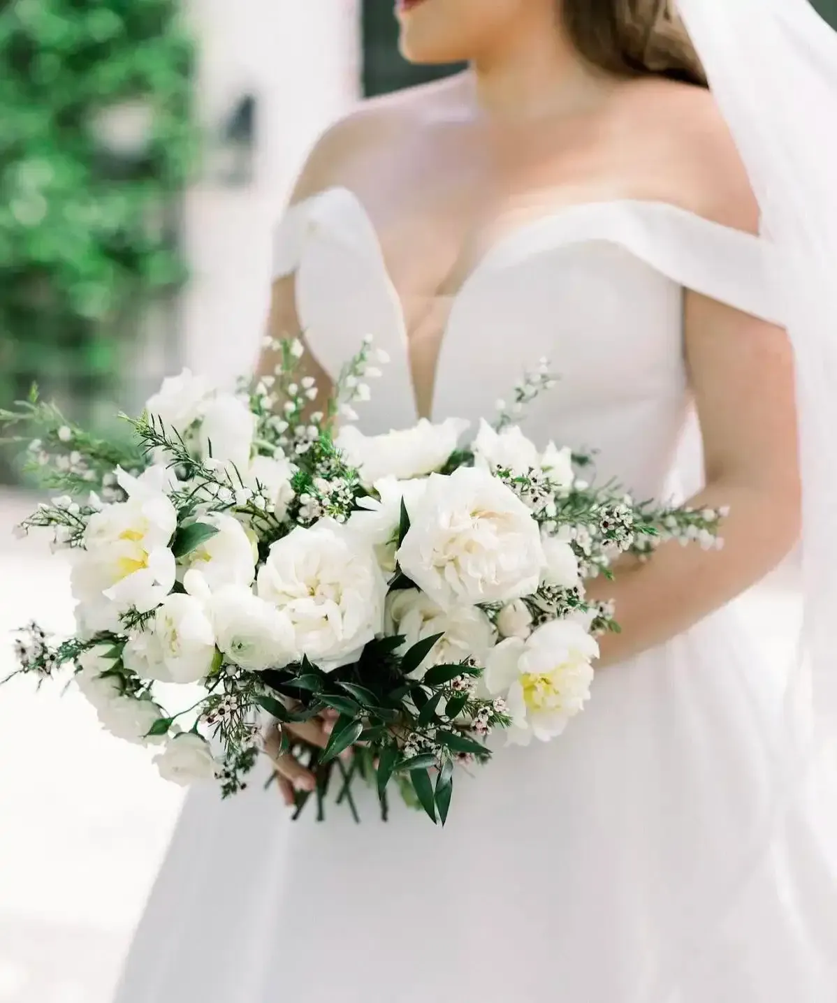 A bride in a white dress is holding a bouquet of white flowers.