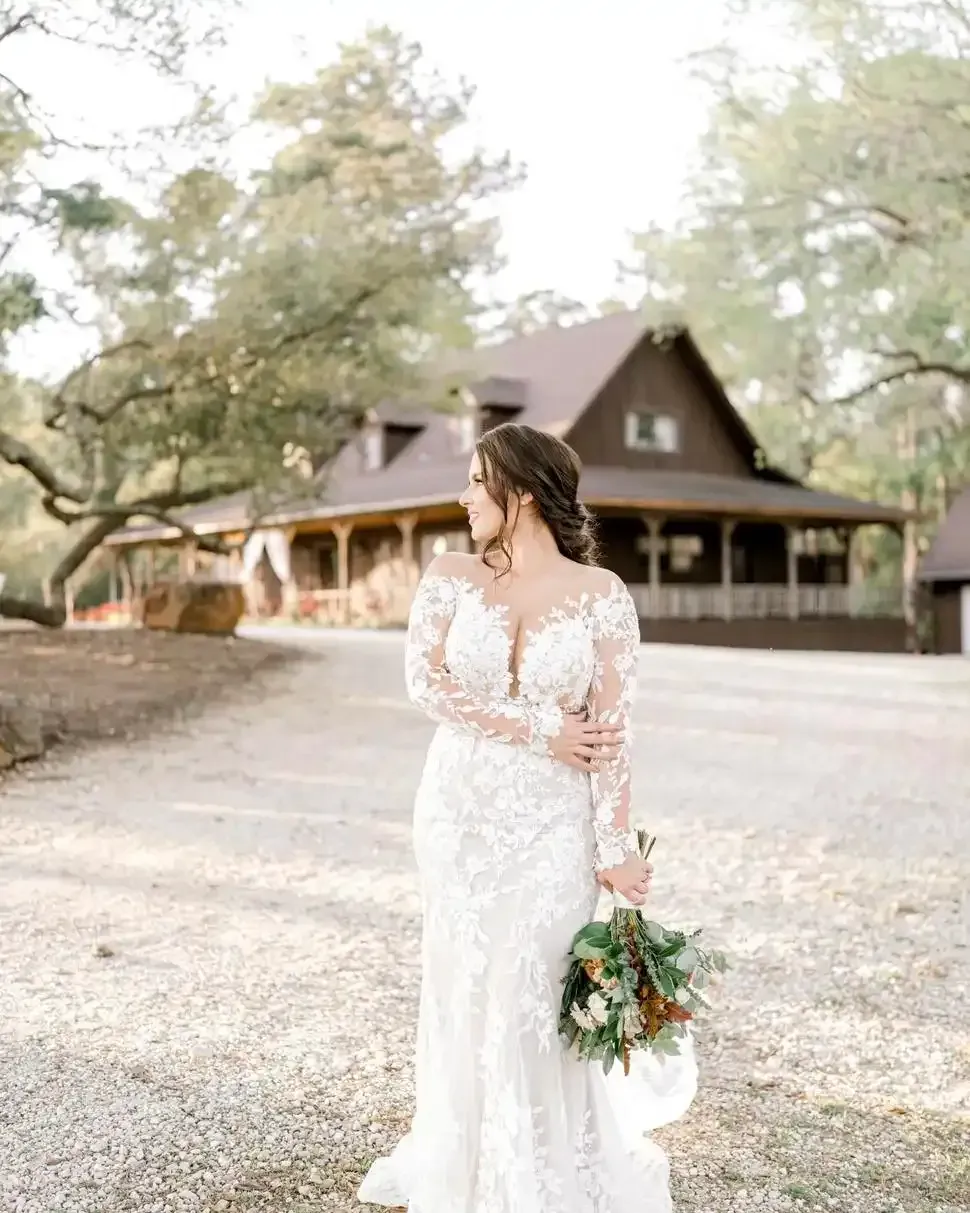 A bride in a wedding dress is standing in front of a house holding a bouquet of flowers.