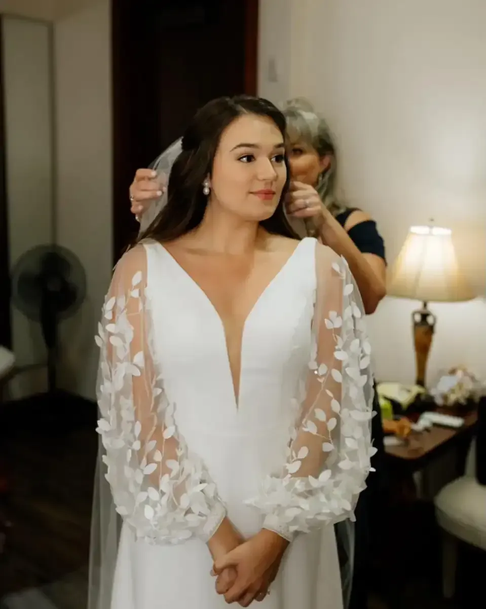A woman is putting a veil on a woman in a white dress.