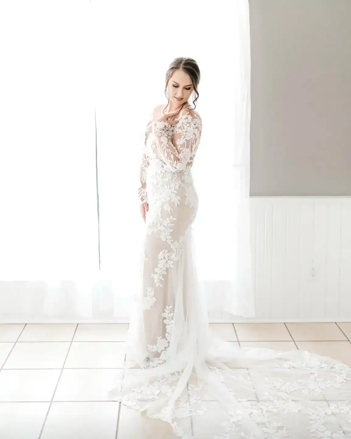 A woman in a wedding dress is standing in front of a window.