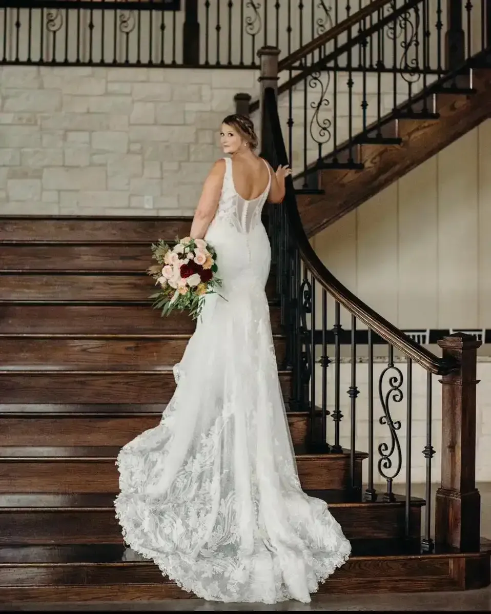 A bride in a wedding dress is standing on a set of wooden stairs holding a bouquet of flowers.