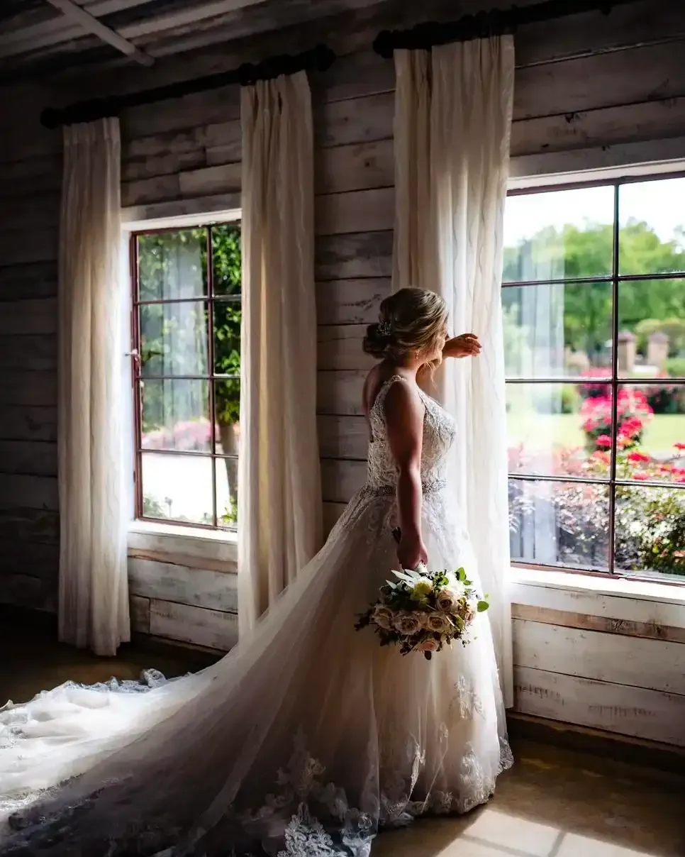 A bride in a wedding dress is standing in front of a window holding a bouquet of flowers.