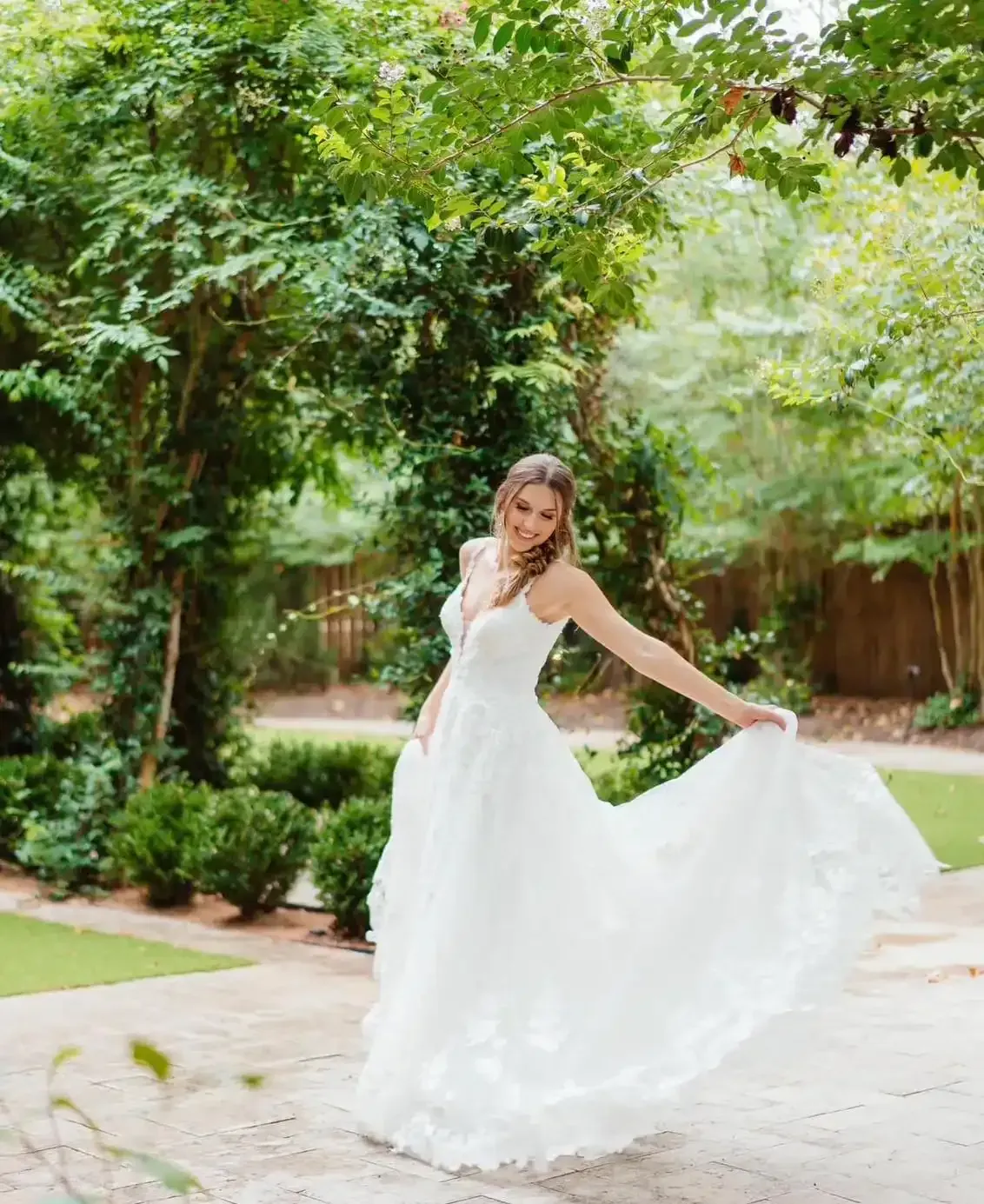 A woman in a white wedding dress is standing in front of trees.
