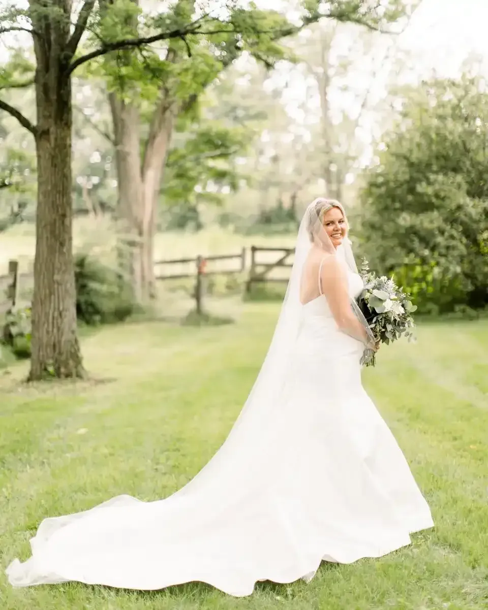 A bride in a wedding dress is standing in the grass holding a bouquet of flowers.