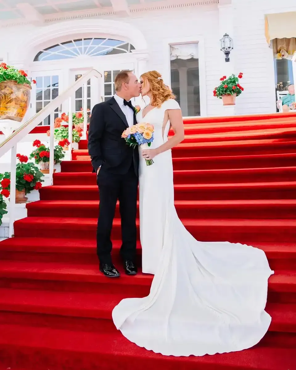 A bride and groom are kissing on a red carpeted staircase.