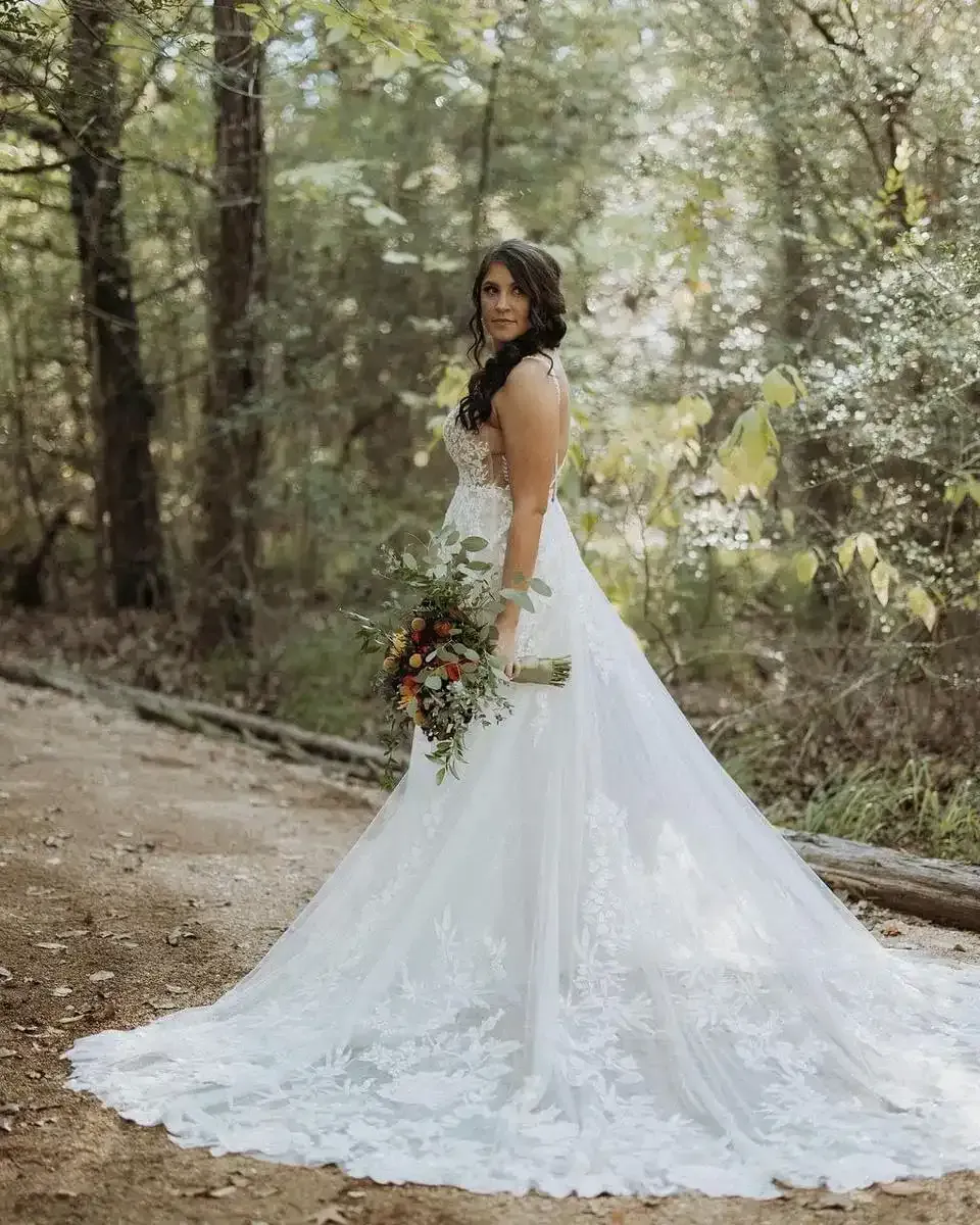 A bride in a wedding dress is standing in the woods holding a bouquet of flowers.
