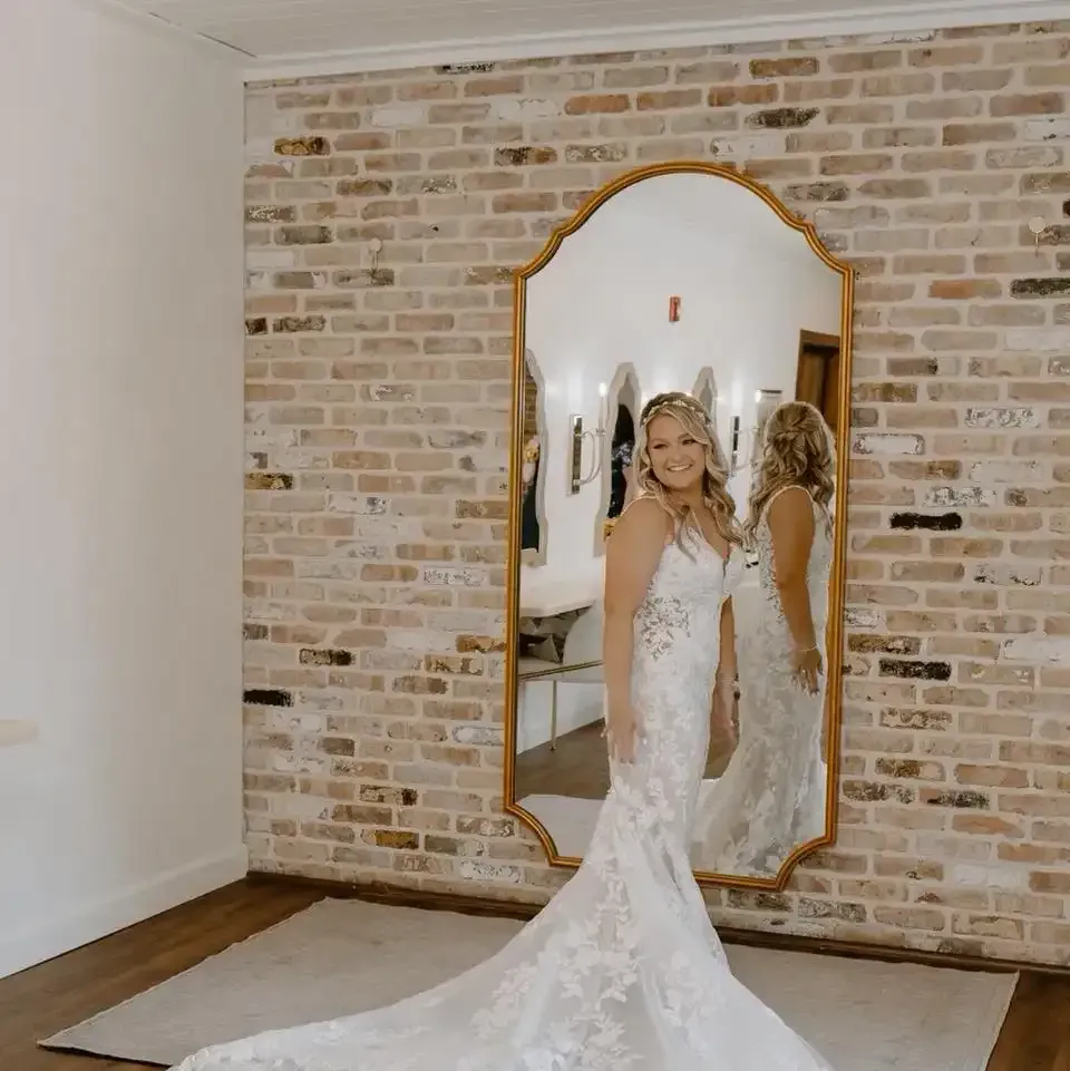 A woman in a wedding dress is standing in front of a large mirror.