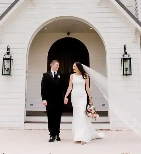 A bride and groom are walking in front of a white building.