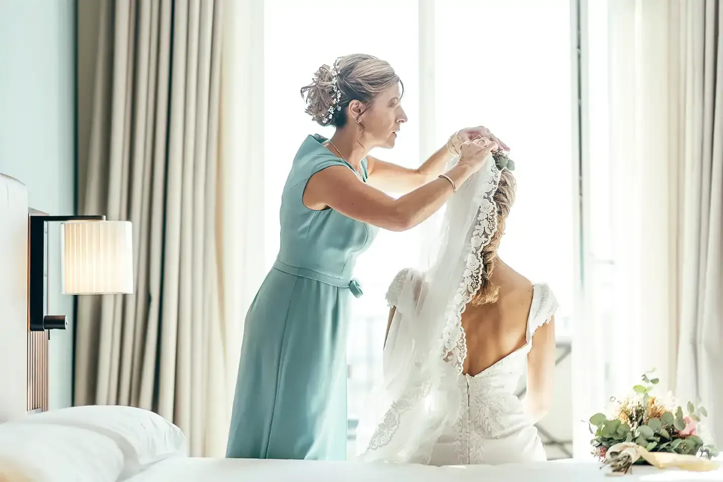 A woman is putting a veil on a bride in a hotel room.