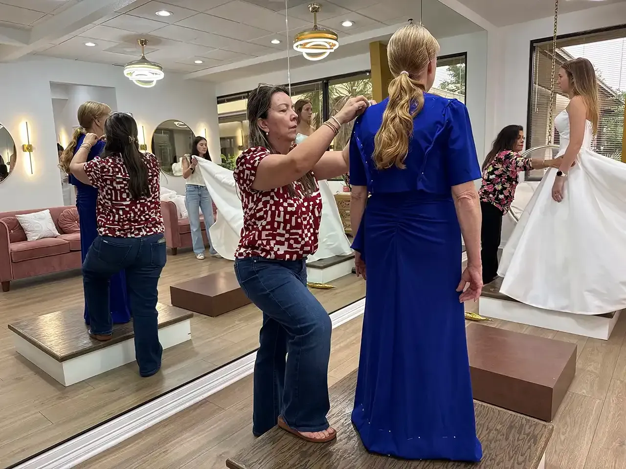 A woman is helping another woman try on a blue dress in a bridal shop.