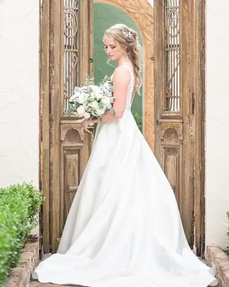 A bride in a white dress is standing in front of a wooden door holding a bouquet of flowers.