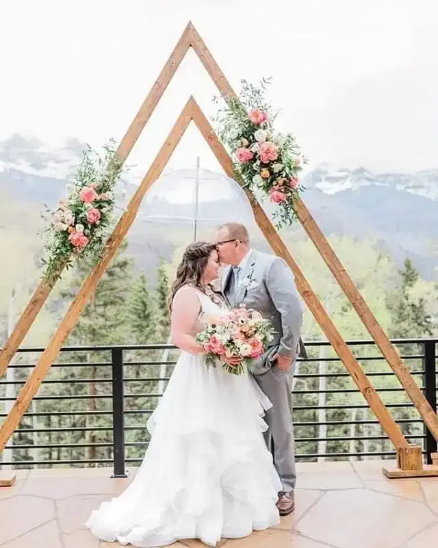 A bride and groom are kissing under a wooden arch.