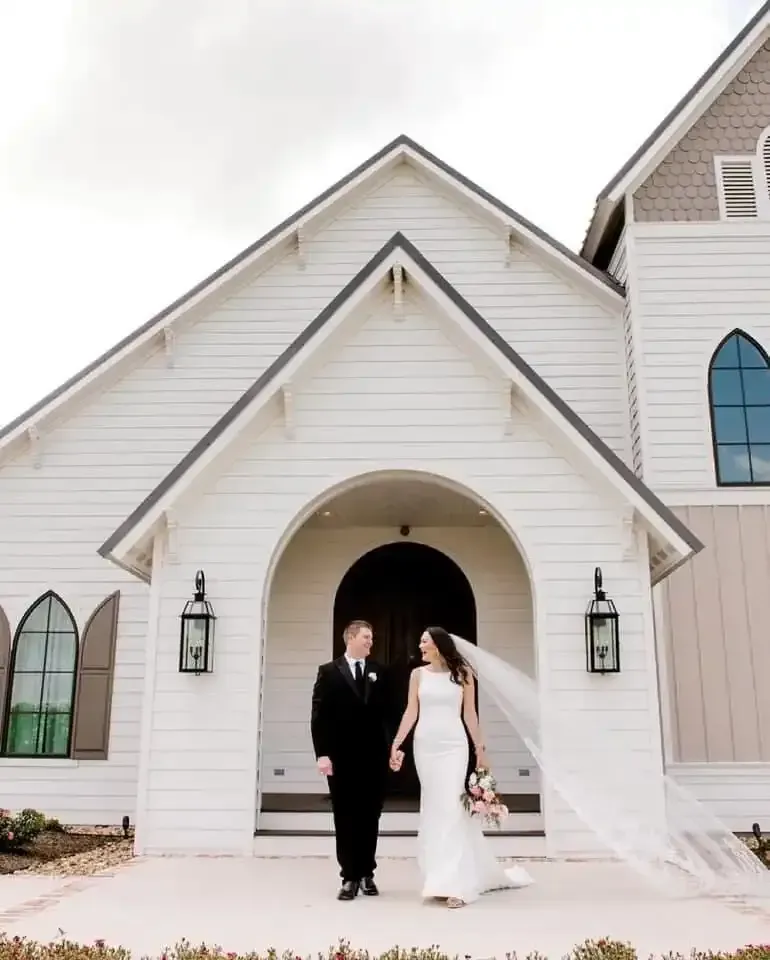 A bride and groom are walking in front of a white church