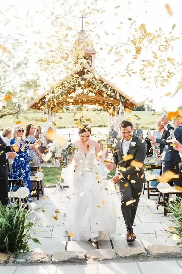 A bride and groom are walking down the aisle while confetti is being thrown at them.