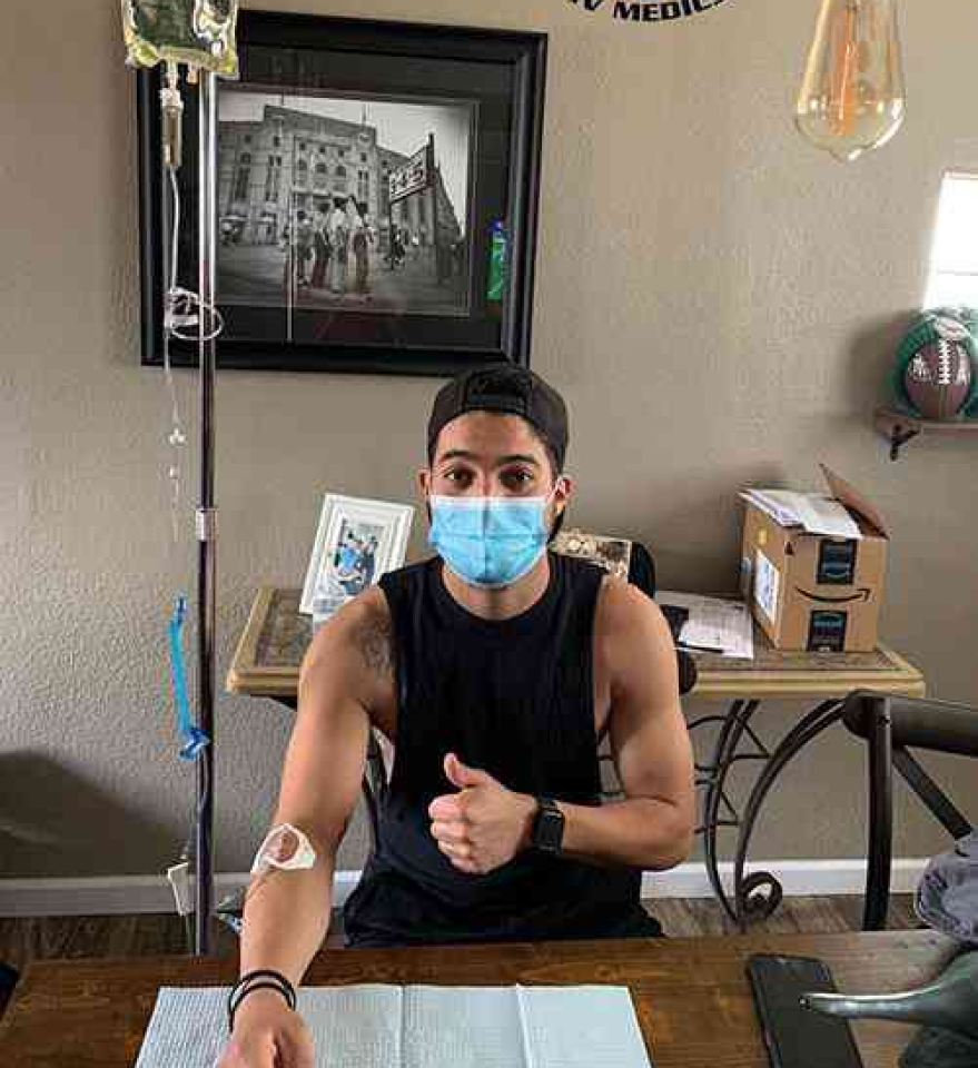 A man wearing a mask is sitting at a table giving a thumbs up.