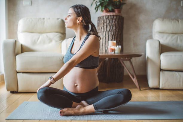 A pregnant woman is sitting on a yoga mat in a living room.