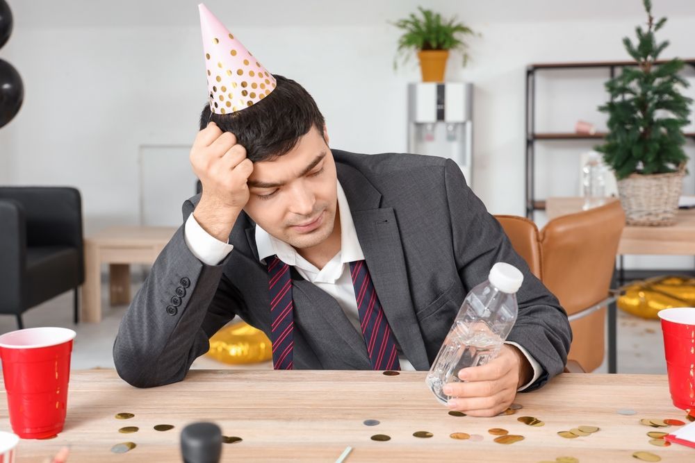 A man in a party hat is sitting at a table with a bottle of water and coins.