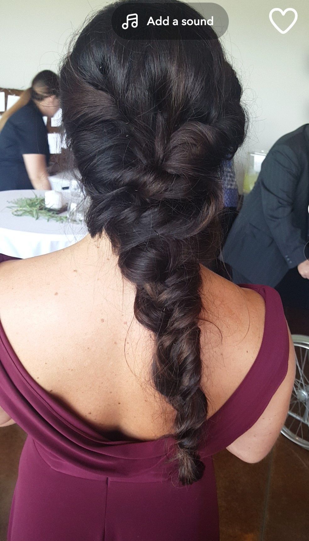 Woman in a burgundy dress with a twisted, dark-brown braid. Back view, indoor setting.