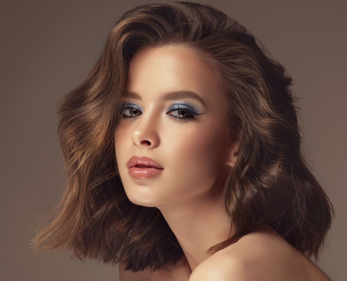 Woman with short, wavy brown hair and blue eyeshadow, looking at the camera.