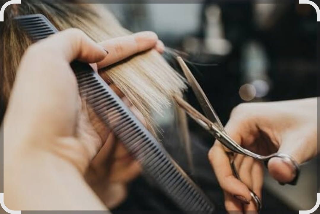 Hairdresser's hands using a comb and scissors to cut blonde hair in a salon.