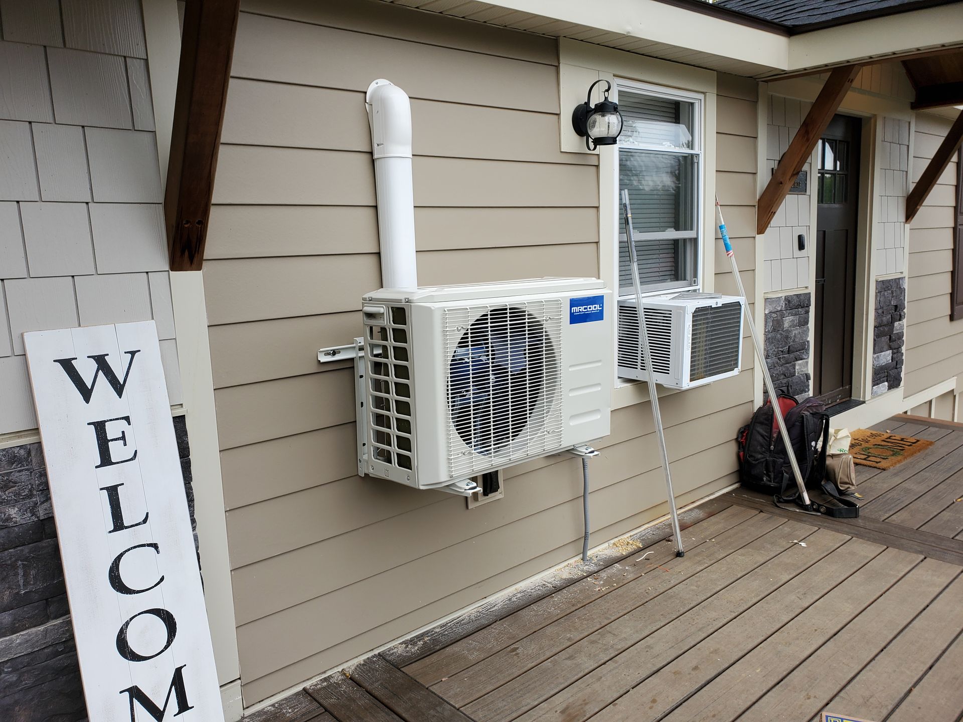 A house with two air conditioners on the side of it and a welcome sign.