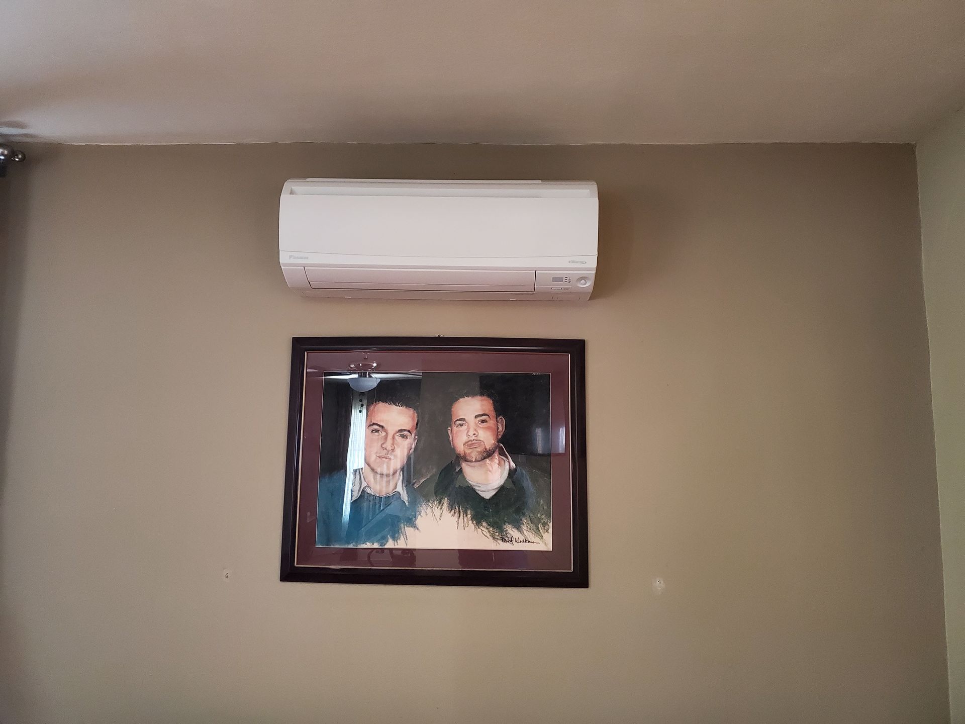 A picture of two men is hanging on a wall next to an air conditioner.