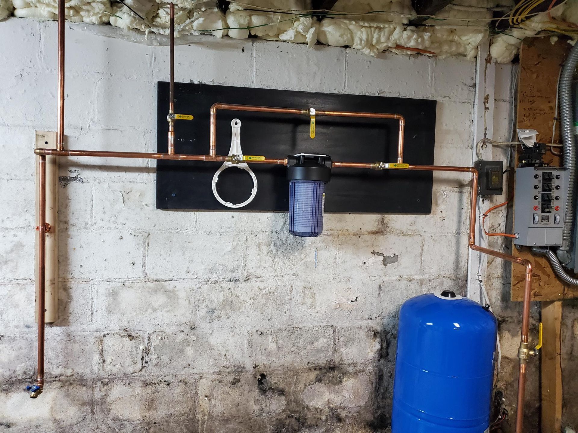 A blue tank is sitting in a basement next to copper pipes