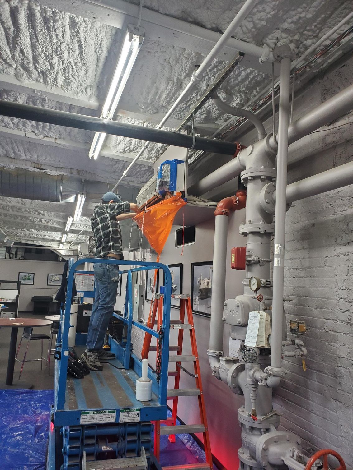 A man is standing on a lift in a room with pipes.