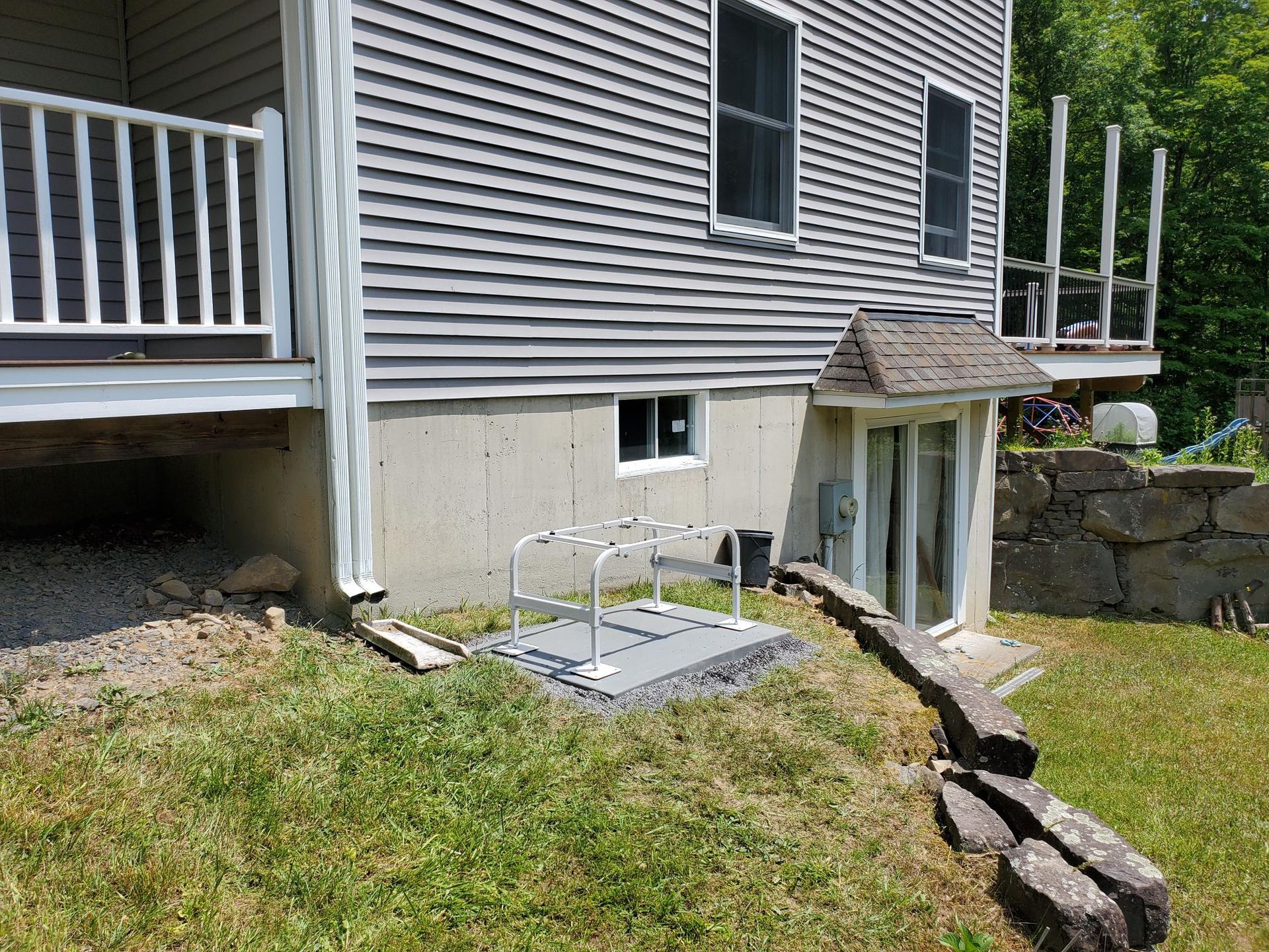 A gray house with a white railing is sitting on top of a grassy hill.
