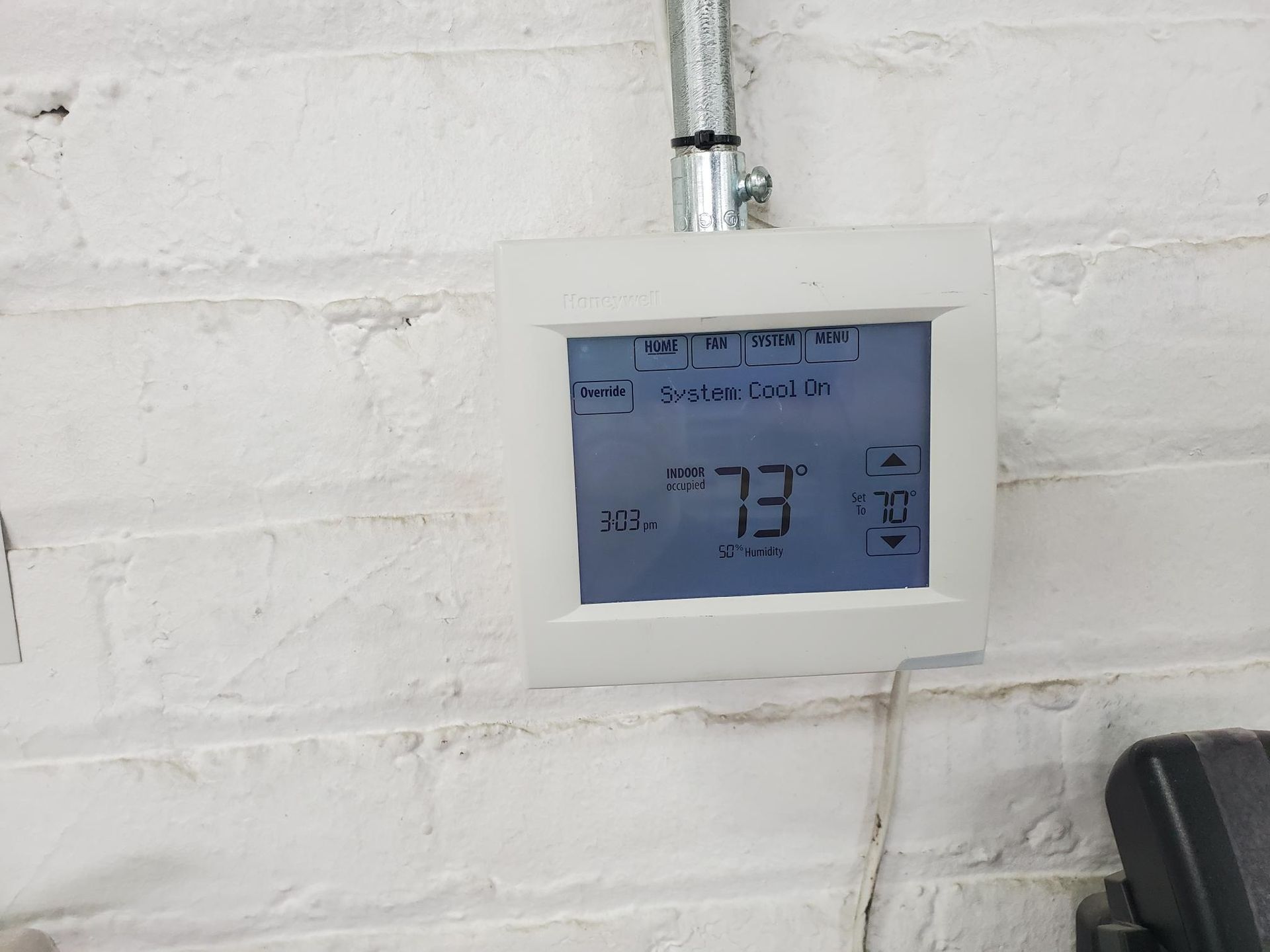 A digital thermostat is hanging on a white brick wall.