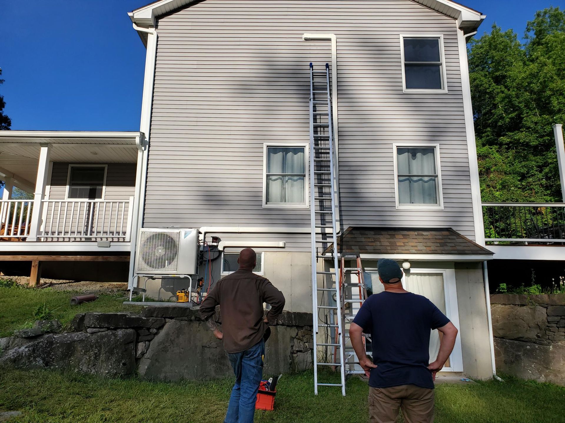 Two men are standing in front of a house with a ladder.