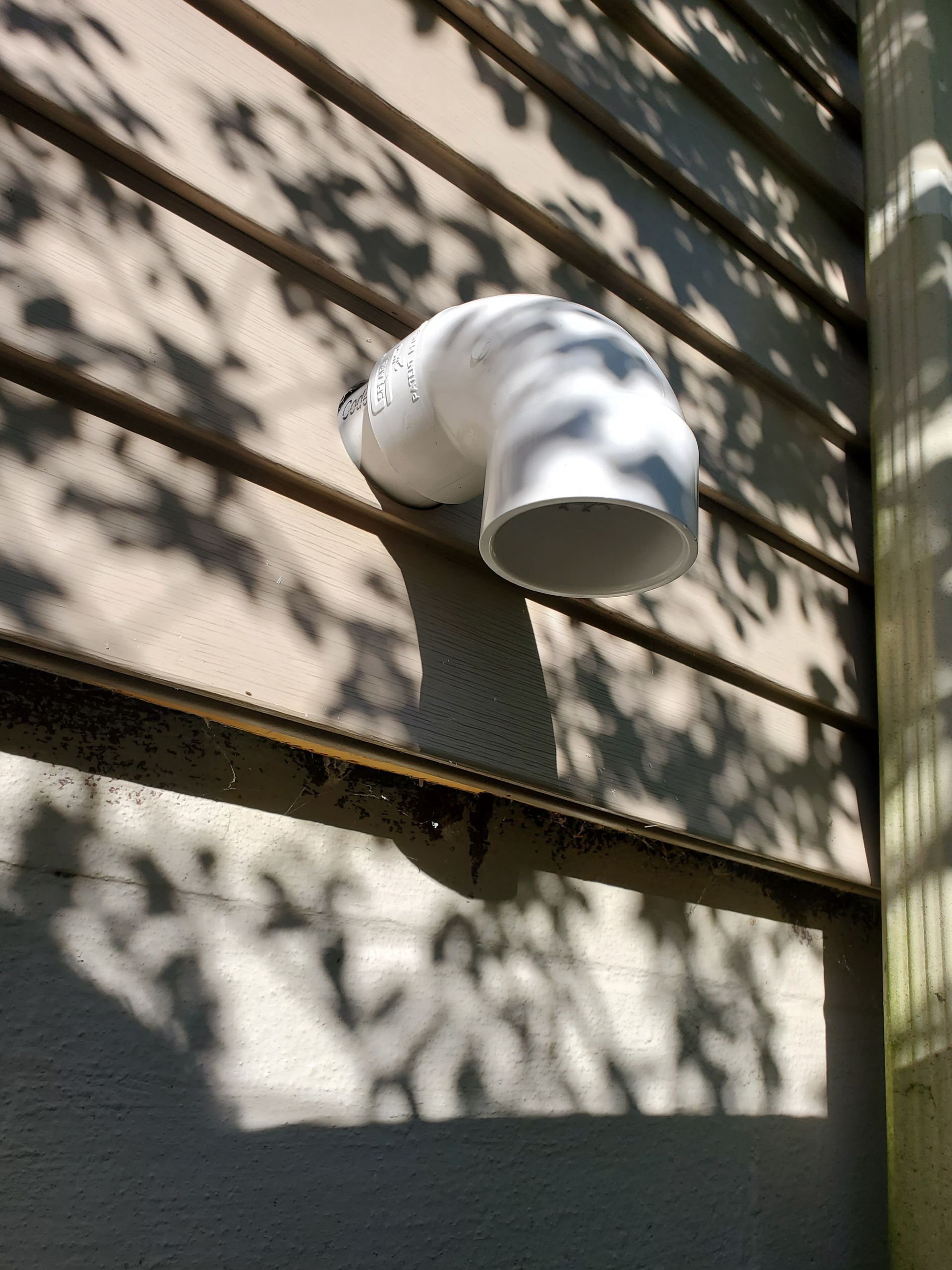 A white pipe is hanging from the side of a building.